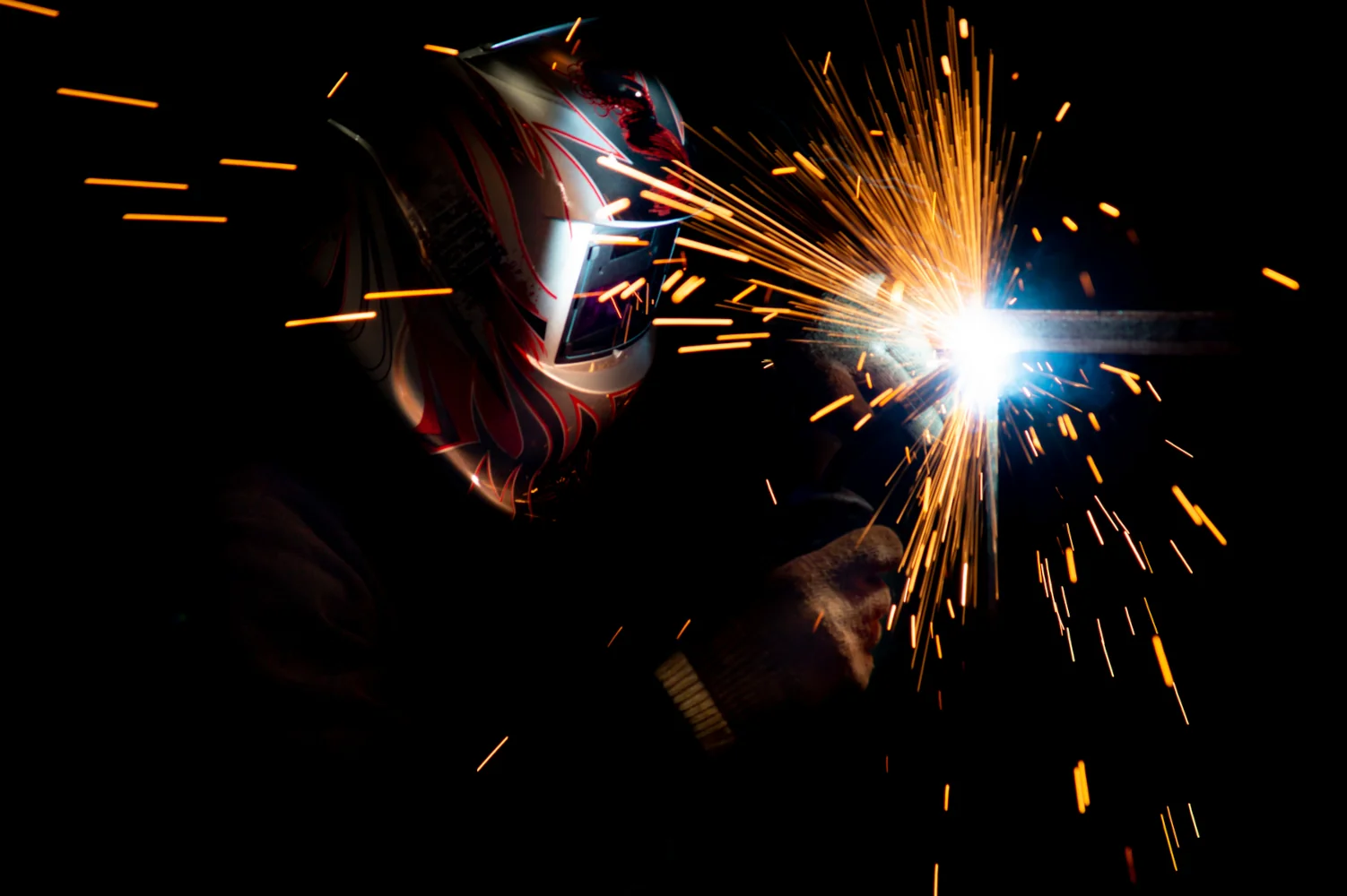 male welder mask performing metal welding photo dark colors sparks flying